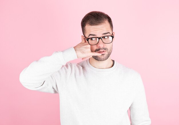 Jovem bonito com barba fazendo gesto de telefone com a mão e os dedos sobre o fundo rosa.