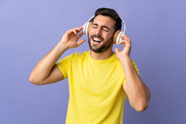 Jovem bonito com barba isolada na parede roxa, ouvir música e cantar