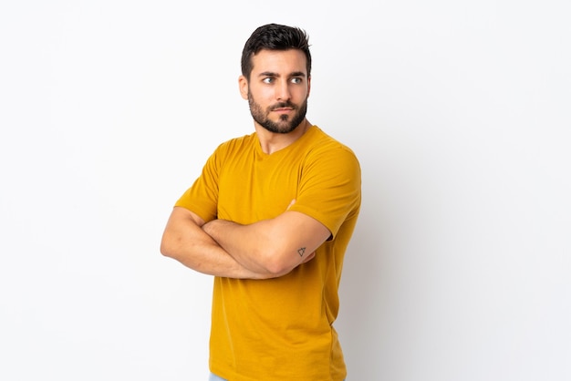 Jovem bonito com barba isolada no fundo branco mantendo os braços cruzados