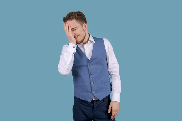 Jovem bonito com barba na camisa branca e colete azul de pé no azul