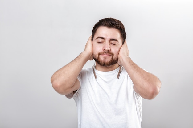 Jovem bonito com barba na camiseta ouvindo música nos fones de ouvido