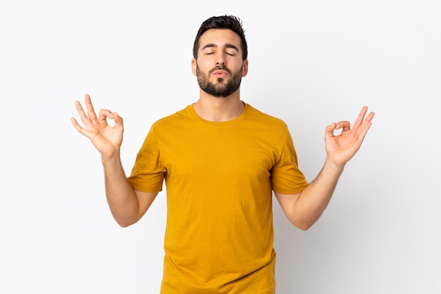 Jovem bonito com barba na parede branca em pose de zen