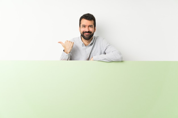 Jovem bonito com barba segurando um grande cartaz vazio verde