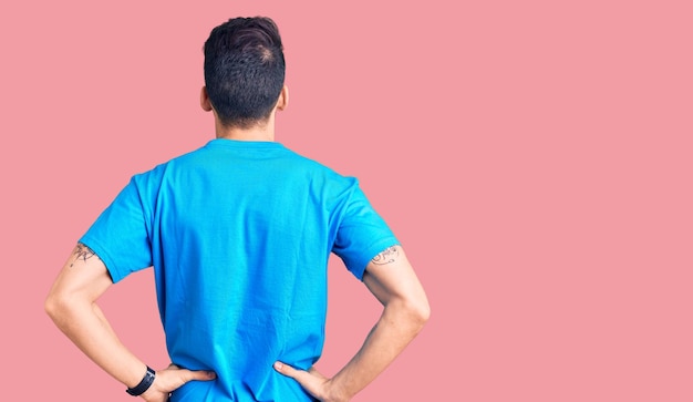 Jovem bonito com barba vestindo camiseta casual em pé para trás olhando para longe com os braços no corpo