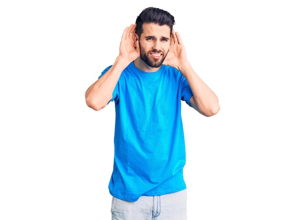 Jovem bonito com barba vestindo camiseta casual tentando ouvir as duas mãos no gesto da orelha curioso para fofocas problema de audição surdo