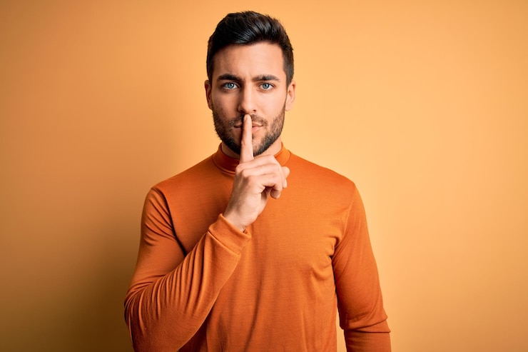 Foto jovem bonito com barba, vestindo suéter casual em pé sobre fundo amarelo, pedindo para ficar quieto com o dedo nos lábios silêncio e conceito secreto