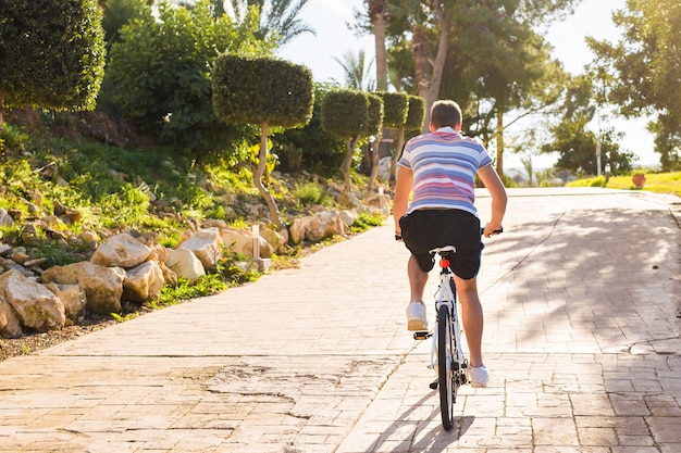 Jovem bonito com bicicleta e capacete no parque em dia ensolarado.