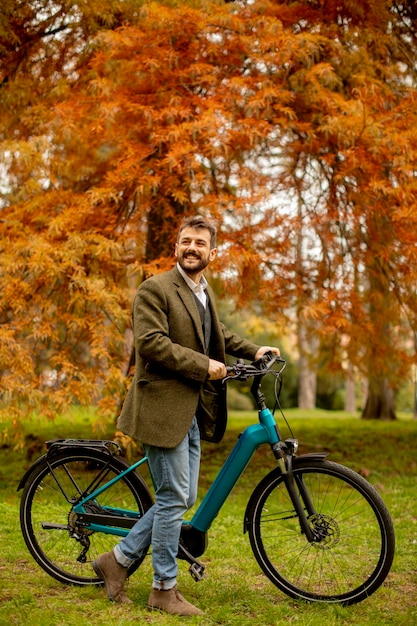 Jovem bonito com bicicleta elétrica no parque outono