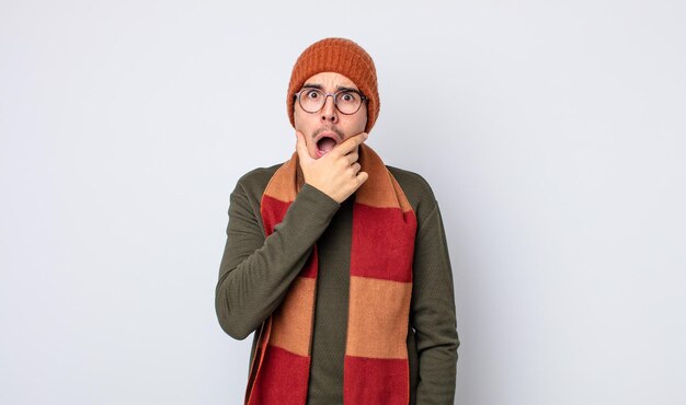 Jovem bonito com boca e olhos bem abertos e mão no queixo. conceito de roupas de inverno