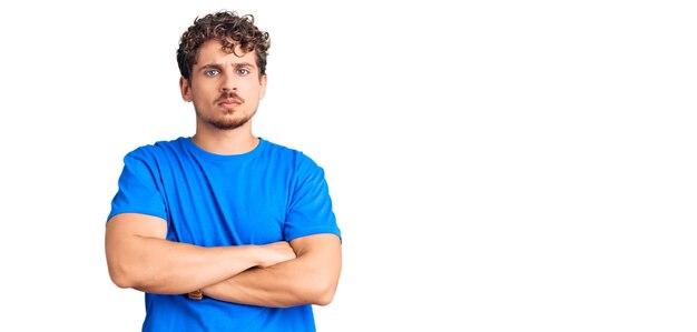 Jovem bonito com cabelo encaracolado, vestindo roupas casuais, expressão de desaprovação nervosa e cética no rosto com pessoa negativa de braços cruzados