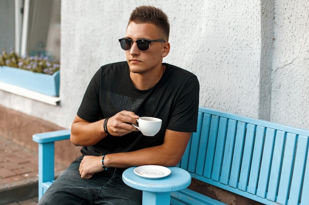 Jovem bonito com café sentado em um banco