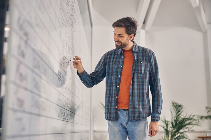 Jovem bonito com camisa quadriculada, escrevendo no quadro do planejador de gráficos e sorrindo