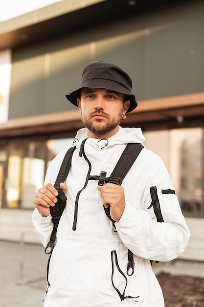 Jovem bonito com chapéu de balde de moda em jaqueta urbana elegante esportiva com mochila anda e viaja na rua