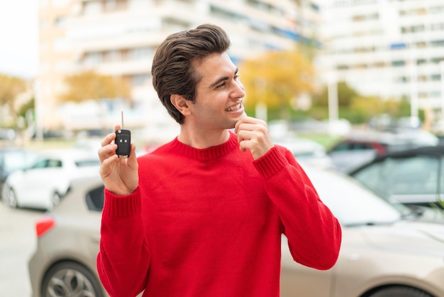 Jovem bonito com chave de carro pensando em uma ideia e olhando de lado