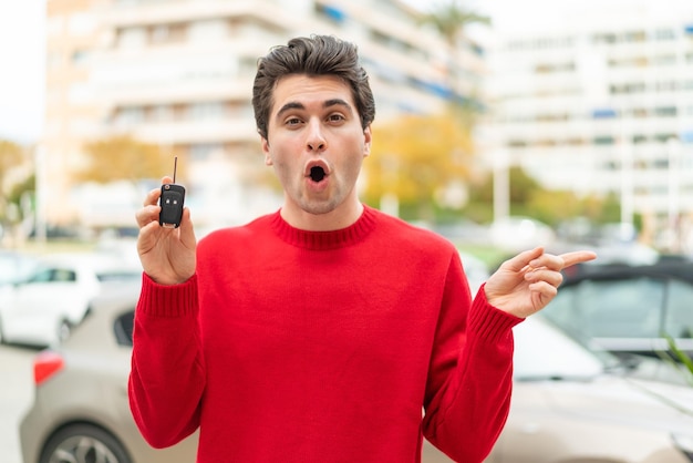 Jovem bonito com chave de carro surpreso e apontando para o lado