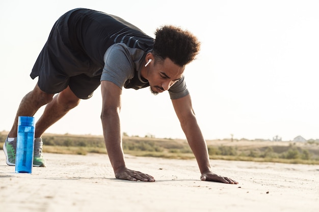 Jovem bonito com esportes fortes ouvindo música com fones de ouvido ao ar livre fazendo exercícios