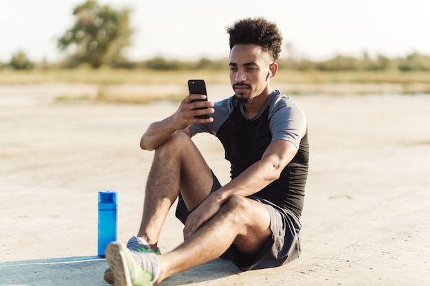 Jovem bonito com esportes fortes ouvindo música com fones de ouvido ao ar livre usando telefone celular