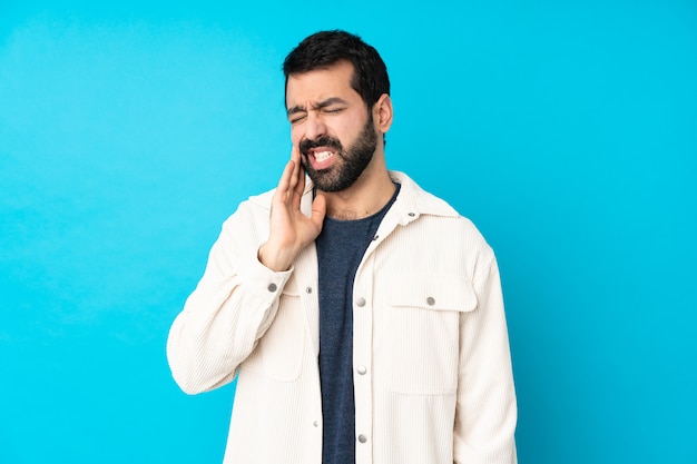 Jovem bonito com jaqueta de veludo branco sobre parede azul isolada com dor de dente