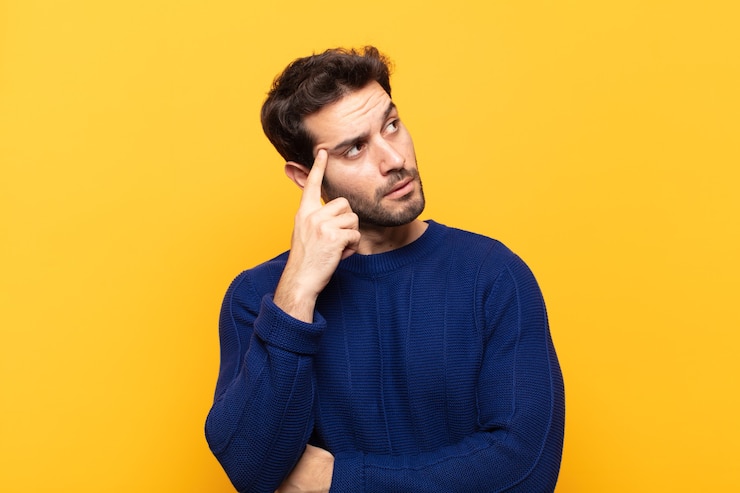 Foto jovem bonito com olhar concentrado, pensando com uma expressão duvidosa, olhando para cima e para o lado