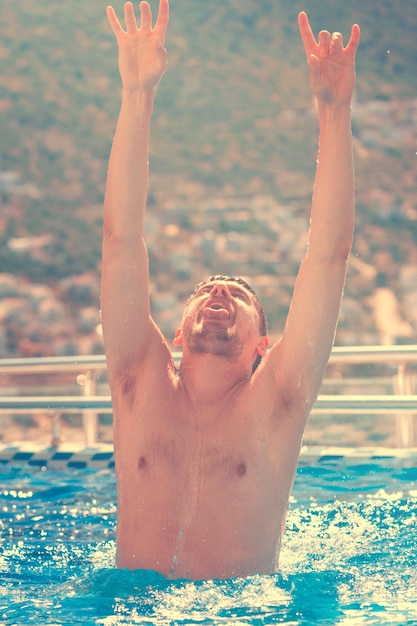 Jovem bonito com os braços erguidos à luz do sol da piscina em tons