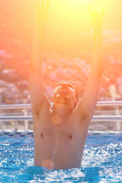 Jovem bonito com os braços erguidos à luz do sol da piscina em tons