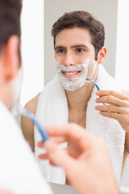 Jovem bonito com reflexão, fazer a barba no banheiro