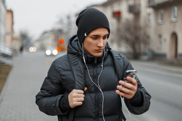 Jovem bonito com roupas de inverno caminhando pela cidade e ouvindo música