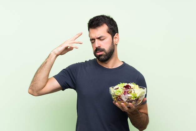 Jovem bonito com salada ao longo da parede verde isolada com expressão de cansado e doente