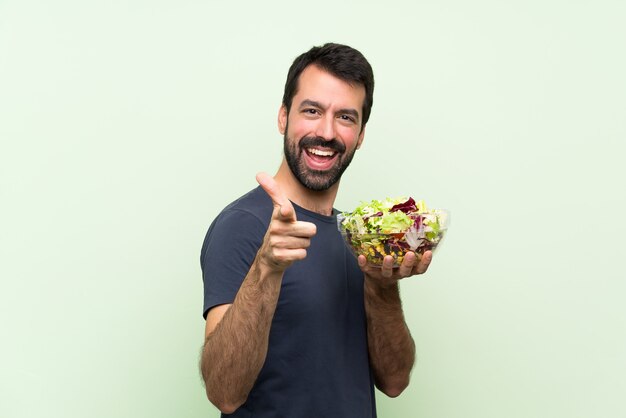 Jovem bonito com salada isolado parede verde apontando para a frente e sorrindo