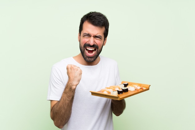 Jovem bonito com sushi ao longo da parede verde frustrado por uma situação ruim