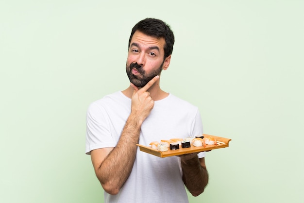 Jovem bonito com sushi sobre pensamento de parede verde isolado