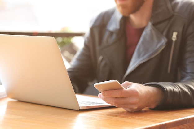 Jovem bonito com telefone e laptop no café