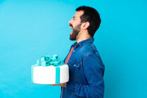 Jovem bonito com um bolo grande sobre azul rindo na posição lateral