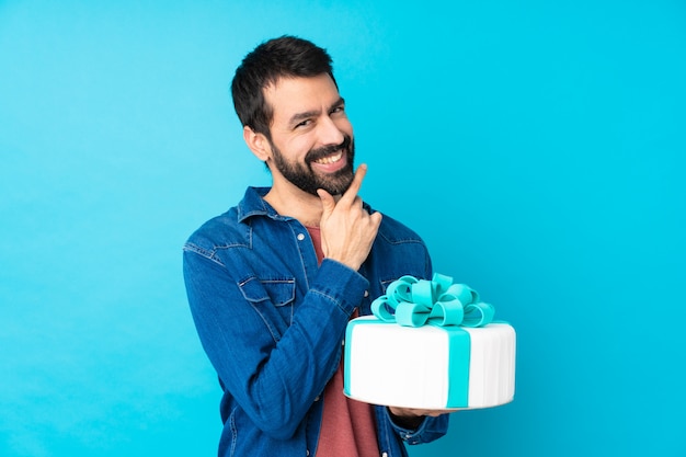 Jovem bonito com um bolo grande sobre parede azul isolado sorrindo