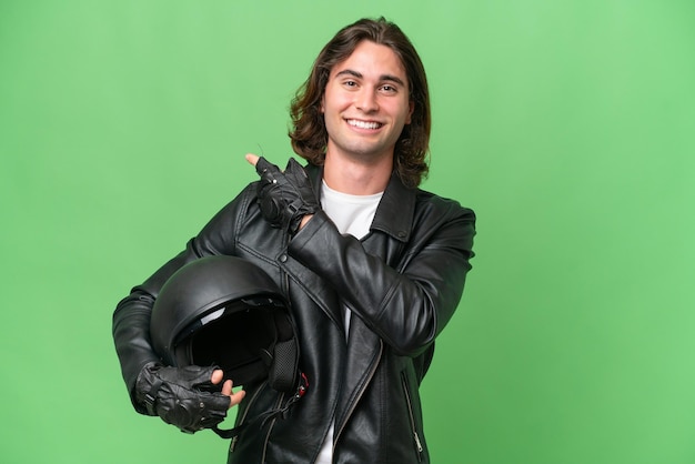 Foto jovem bonito com um capacete de moto isolado no fundo croma verde apontando para trás