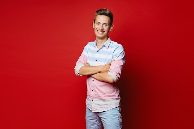 Jovem bonito com um penteado elegante na camisa e shorts posando com as mãos postas sobre o fundo vermelho