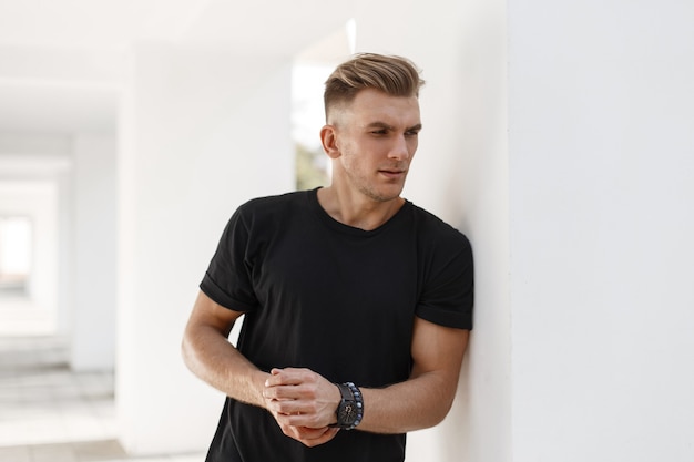 Jovem bonito com um penteado estiloso em uma camiseta preta na rua