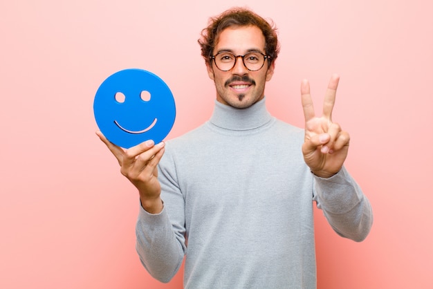 Jovem bonito, com um rosto sorridente contra parede plana-de-rosa