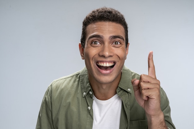 Jovem bonito com um sorriso cheio de dentes apontando para cima com o dedo