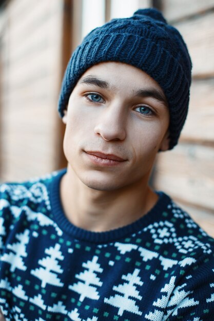 Jovem bonito com um toque de inverno e uma camisola de malha perto da velha casa de madeira