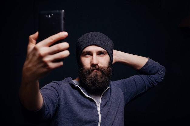 Jovem bonito com uma barba com um capuz tirando uma selfie