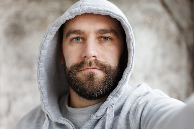 Jovem bonito com uma barba em uma camisa quadriculada se fazendo, sorrindo, sobre um fundo cinza