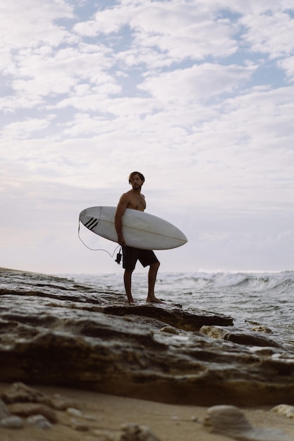 Jovem bonito com uma prancha de surf no oceano.