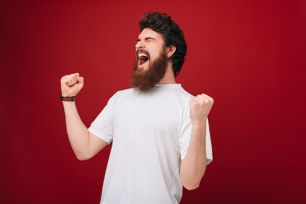 Jovem bonito comemorando para o sucesso com os braços levantados e os olhos fechados. Conceito vencedor.