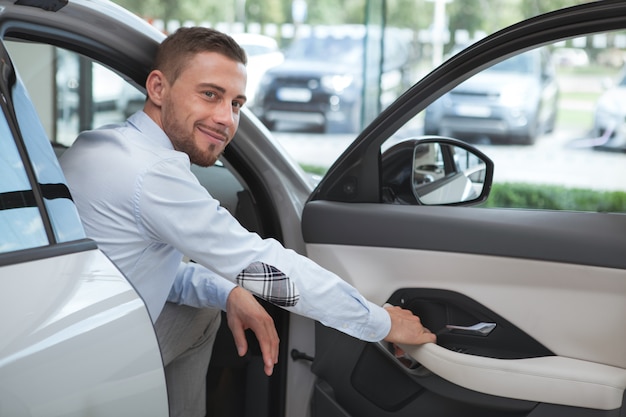 Jovem bonito comprando um carro novo no salão da concessionária