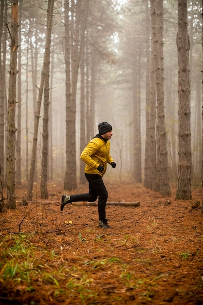 Jovem bonito correndo na floresta de outono e se exercitando para a maratona de corrida em trilha