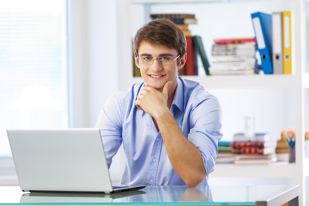 Jovem bonito de óculos usando laptop