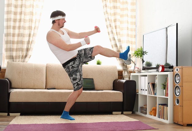 Jovem bonito de short e colete segura halteres rosa na mão Assistir aulas de TV combates individuais está praticando recepções de sensei one home fitness treinamento interno educação independente remotamente