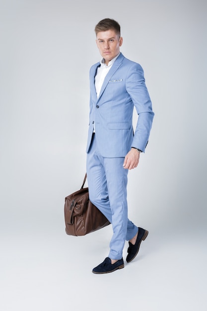 Jovem bonito de terno azul segurando uma bolsa de couro
