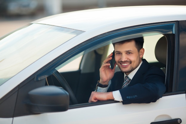 jovem bonito de terno falando ao telefone, sentado no carro